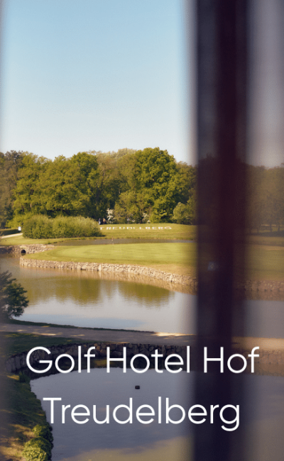 Blick durch ein Fenster auf einen Golfplatz mit einem Teich und grünen Bäumen im Hintergrund. Unten steht der Text: „Golfhotel Hof Treudelberg“.